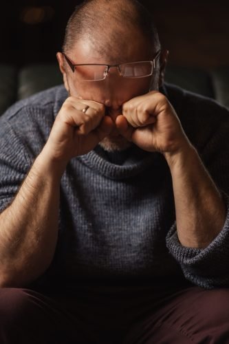 A man rubs his eyes in front of a book. Pain in the eyes, fatigue, headache.